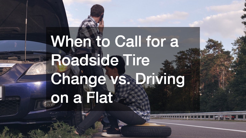 woman fixing a car's flat tire on the side of a road while a man is making a phone call